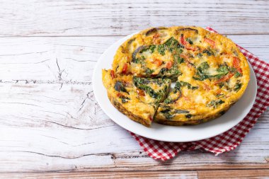 Beyaz ahşap masada ıspanak, domates, soğan ve biberden yapılmış İtalyan Frittata. Boşluğu kopyala