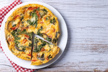 Beyaz ahşap masada ıspanak, domates, soğan ve biberden yapılmış İtalyan Frittata.