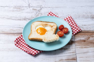 Domatesli yumurta, kalp şeklinde ekmek ve ahşap masada kızarmış ekmek ile Sevgililer Günü kahvaltısı.