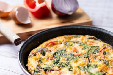 Beyaz ahşap masada ıspanak, domates, soğan ve biberden yapılmış İtalyan Frittata.