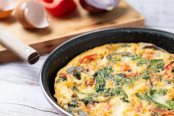 Beyaz ahşap masada ıspanak, domates, soğan ve biberden yapılmış İtalyan Frittata.