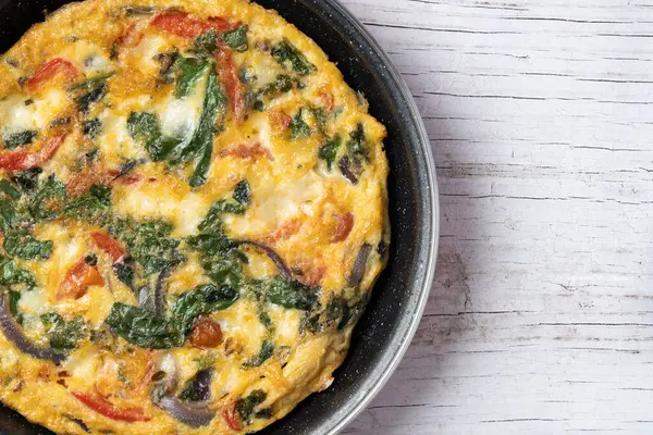 Beyaz ahşap masada ıspanak, domates, soğan ve biberden yapılmış İtalyan Frittata. Üst Manzara. Boşluğu kopyala