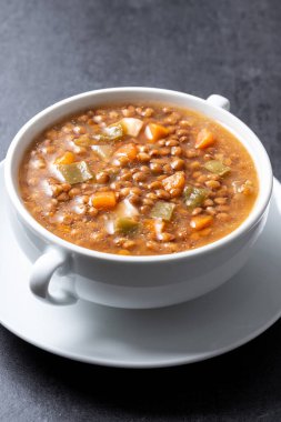 Siyah arka planda sebzeli mercimek çorbası.