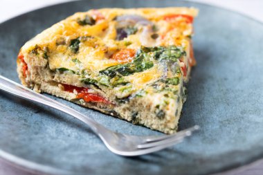 Beyaz ahşap masada ıspanak, domates, soğan ve biberden yapılmış İtalyan Frittata.