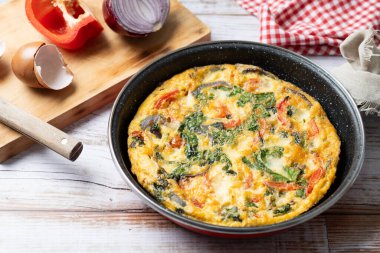 Beyaz ahşap masada ıspanak, domates, soğan ve biberden yapılmış İtalyan Frittata.