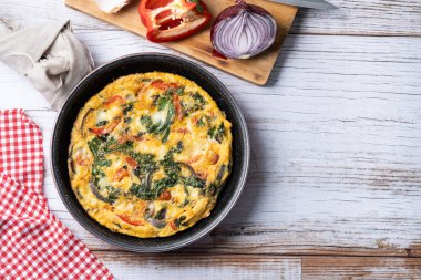 Beyaz ahşap masada ıspanak, domates, soğan ve biberden yapılmış İtalyan Frittata.