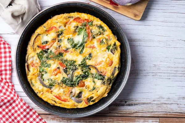 Beyaz ahşap masada ıspanak, domates, soğan ve biberden yapılmış İtalyan Frittata.