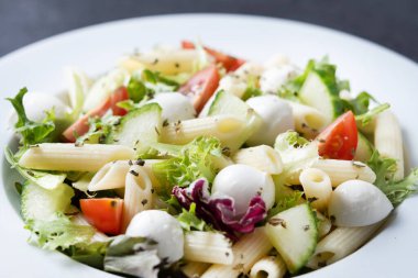 Sebzeli makarna salatası ve siyah arka planda mozzarella peyniri.