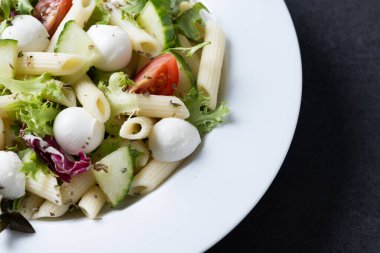 Sebzeli makarna salatası ve siyah arka planda mozzarella peyniri.
