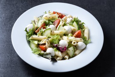 Sebzeli makarna salatası ve siyah arka planda mozzarella peyniri.