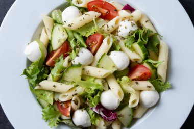 Sebzeli makarna salatası ve siyah arka planda mozzarella peyniri.