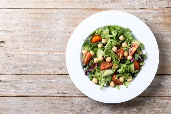 健康的鹰嘴豆沙拉 配上西红柿 生菜和黄瓜 放在木制桌子上 免版税图库图片