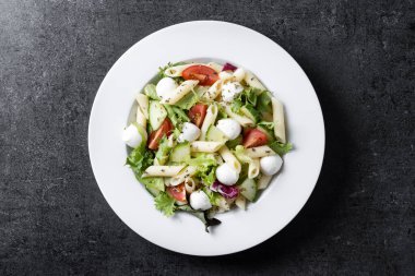Sebzeli makarna salatası ve siyah arka planda mozzarella peyniri.