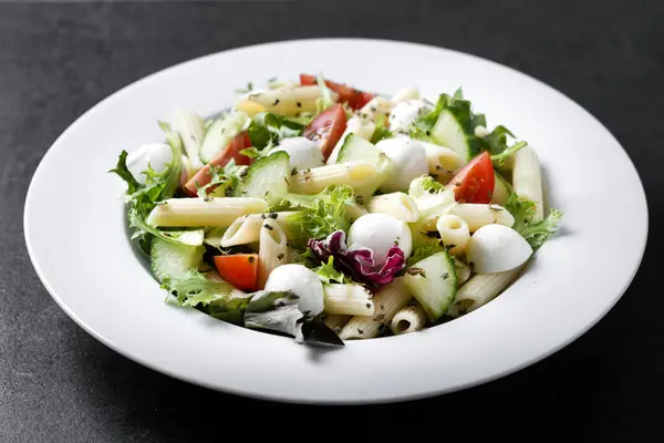 配菜的意大利面沙拉和黑色背景的莫扎拉奶酪 免版税图库图片