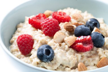Beyaz arka planda yulaf lapası, ahududu, yaban mersini ve badem. Kapat.