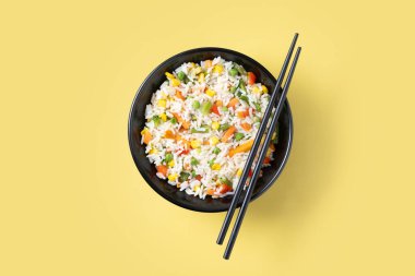 Sarı arka planda siyah kasede sebzeli beyaz pirinç. Üst görünüm