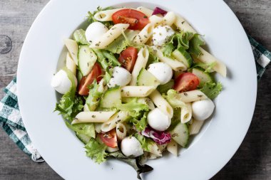 Sebzeli makarna salatası ve ahşap masada mozzarella peyniri. Kapat.