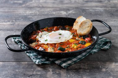Domatesli sebze pisto manchego, kabak, biber, soğan, patlıcan ve yumurta, ahşap masada izole edilmiş tavada servis edilir.
