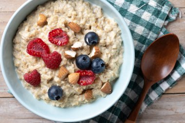 Ahududulu yulaf lapası, ahududu ve badem kasesi ahşap masada.