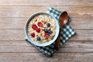 Ahududulu yulaf lapası, ahududu ve badem kasesi ahşap masada.