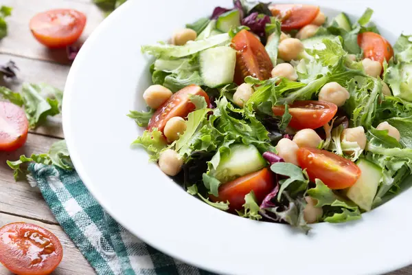 Tahta masada domates, marul ve salatalıklı sağlıklı nohut salatası.