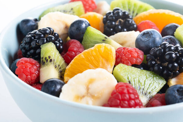 Фруктовый салат с киви, мандарином, бананом, малиной, ежевикой, черникой в голубой миске изолирован на белом фоне. Закрыть
