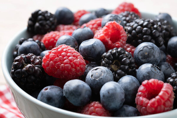 Fresh assortment berries in bowl on wooden table. Close up