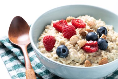 Beyaz arka planda yulaf lapası, ahududu, yaban mersini ve badem.