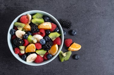 Siyah arka planda mavi bir kasede meyve salatası. Üst Manzara. Boşluğu kopyala