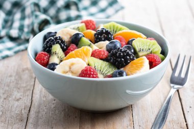 Ahşap masada mavi bir kasede meyve salatası.