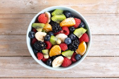 Ahşap masada mavi bir kasede meyve salatası. Üst görünüm