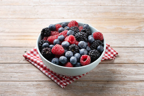 Fresh assortment berries in bowl on wooden table