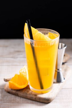 Ahşap masa ve siyah arka planda turuncu votka kokteyli.