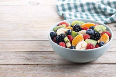 Ahşap masada mavi bir kasede meyve salatası. Boşluğu kopyala