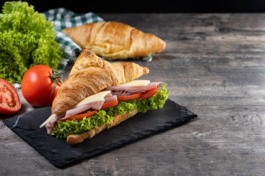 Ahşap masada jambonlu, peynirli ve sebzeli kruvasan. Boşluğu kopyala