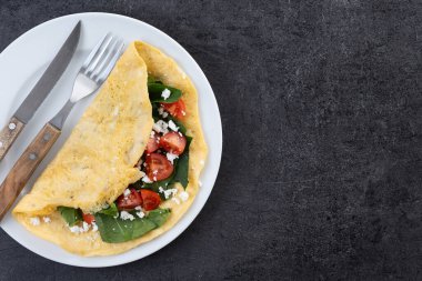Doldurulmuş domatesli omlet ve siyah arka planda ıspanak. Üst Manzara. Boşluğu kopyala