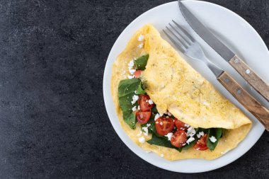 Doldurulmuş domatesli omlet ve siyah arka planda ıspanak. Üst Manzara. Boşluğu kopyala