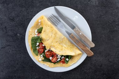 Doldurulmuş domatesli omlet ve siyah arka planda ıspanak.