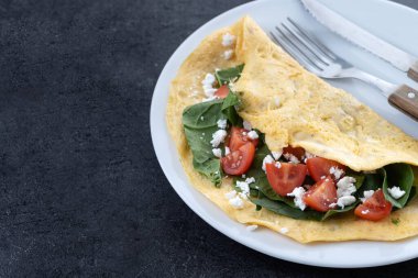 Doldurulmuş domatesli omlet ve siyah arka planda ıspanak. Boşluğu kopyala