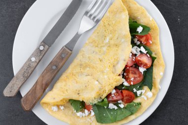 Doldurulmuş domatesli omlet ve siyah arka planda ıspanak.