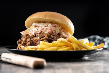 Lahana salatalı domuz sandviçi ve tahta masada patates kızartması.