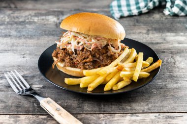 Lahana salatalı domuz sandviçi ve tahta masada patates kızartması.