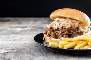 Lahana salatalı domuz sandviçi ve tahta masada patates kızartması.