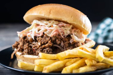 Lahana salatalı domuz sandviçi ve tahta masada patates kızartması.