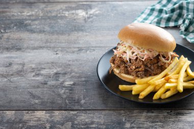 Lahana salatalı domuz sandviçi ve ahşap masada patates kızartması.