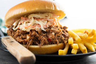 Lahana salatalı domuz sandviçi ve ahşap masada patates kızartması.