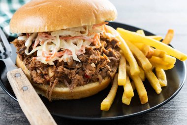 Lahana salatalı domuz sandviçi ve ahşap masada patates kızartması.