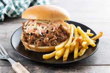 Lahana salatalı domuz sandviçi ve ahşap masada patates kızartması.