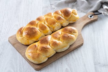 Geleneksel Paskalya örülmüş ekmek. Beyaz ahşap masada Tsoureki örgüsü