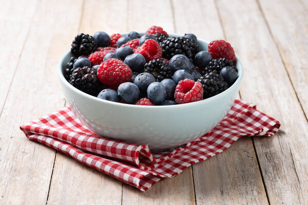 Fresh assortment berries in bowl on wooden table